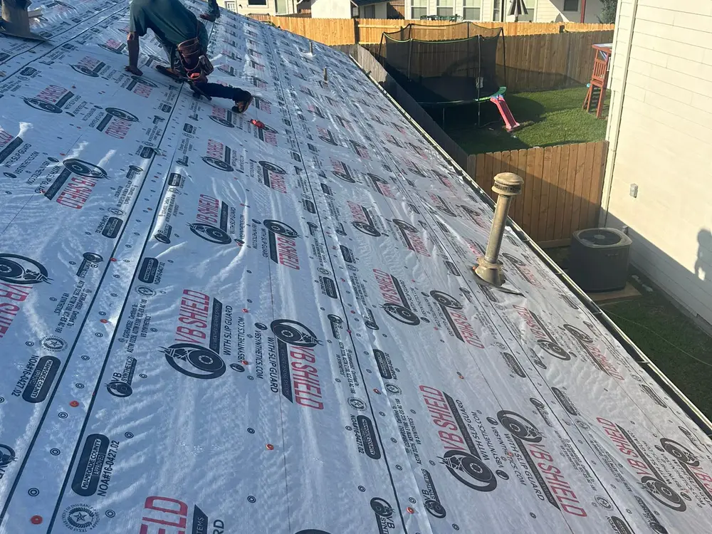 Roofer laying synthetic underlayment across a roof deck