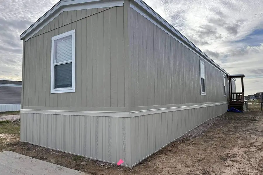 Manufactured home wrapped in tan vertical panel siding with matching skirting