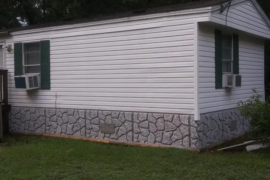 White lap siding with green shutters and stone-pattern skirting on a manufactured home